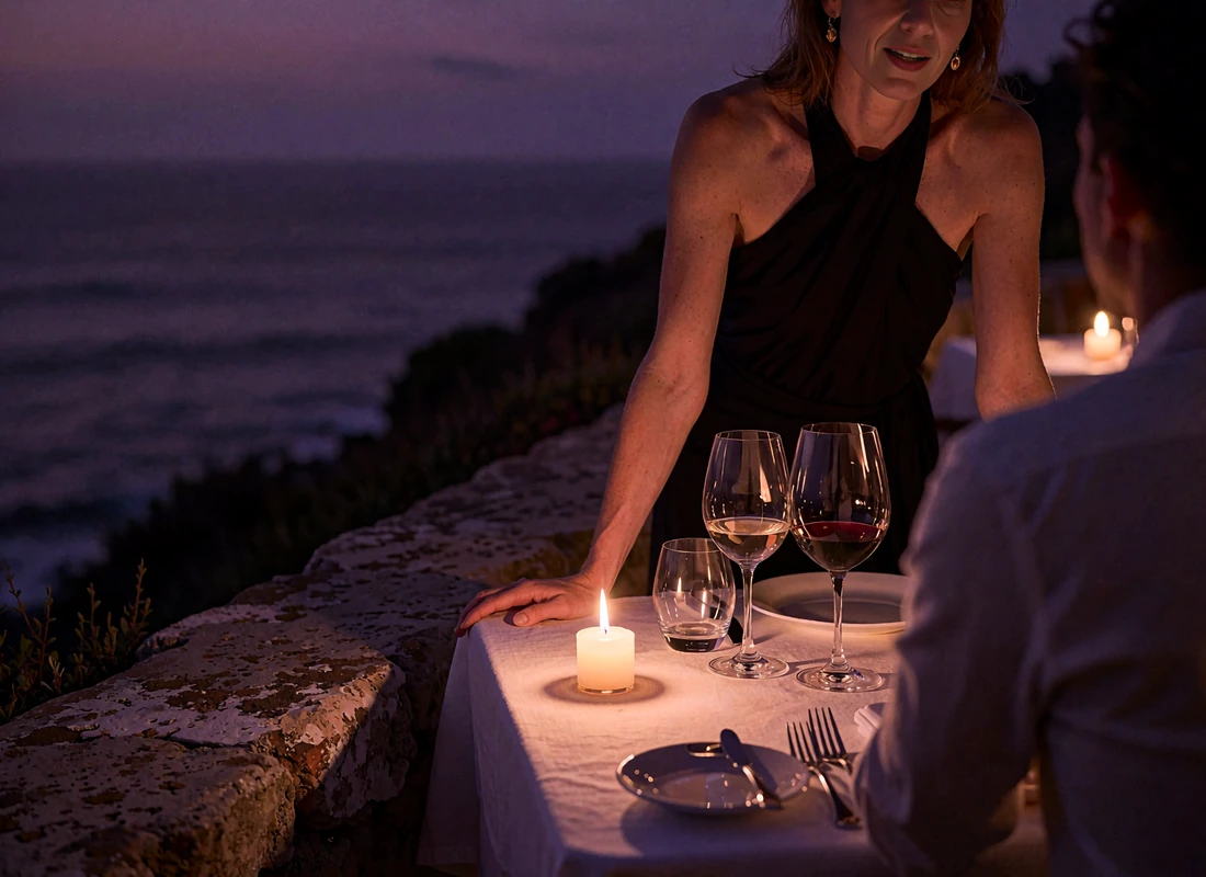 Candlelit two-top table at a cliffside restaurant terrace overlooking the darkened Pacific horizon at dusk