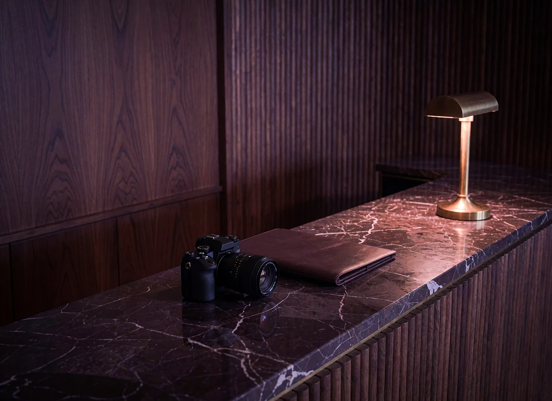 Dim hotel concierge alcove with dark marble counter, a brass lamp and a closed leather folio